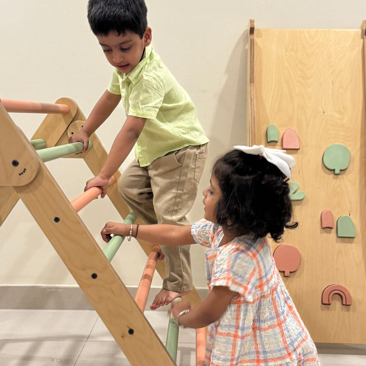 Two children playing on a wooden climbing toy indoors.