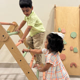 Two children playing on a wooden climbing toy indoors.